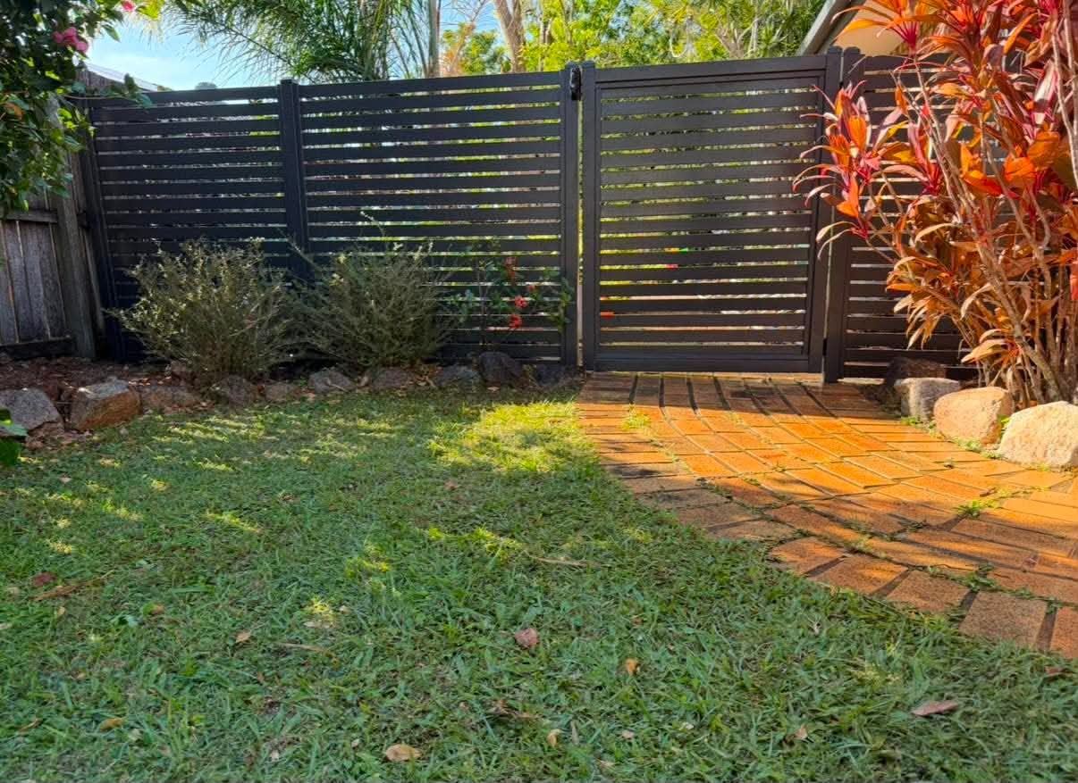 Dark Colorbond boundary fence and gate framed by garden planting