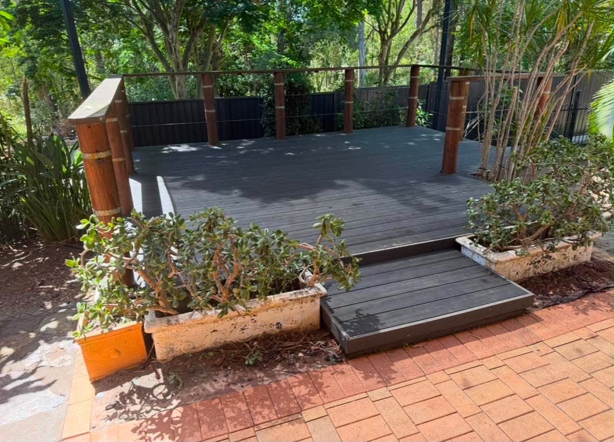 Composite deck with wide steps, hardwood posts and wire balustrade set among established garden planting
